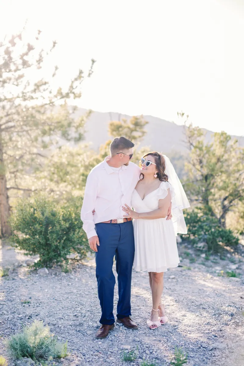 Man kissing his fiancee's cheek while she smiles under a long veil
