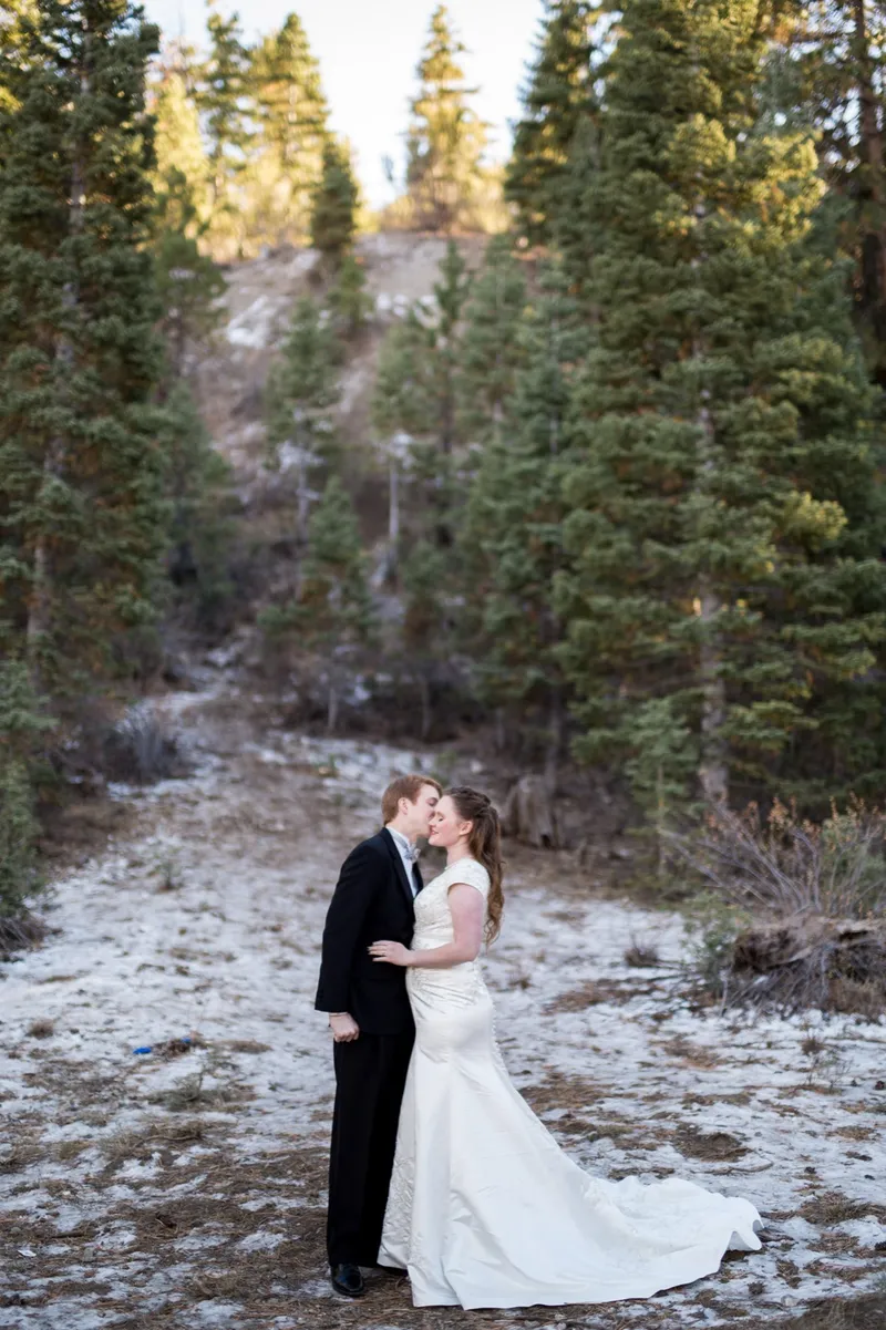Couple kissing among the pines with snow scattered across the ground