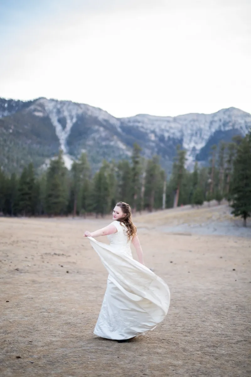 Bride holding her skirt out as she turns in the meadow below the snow topped ridge