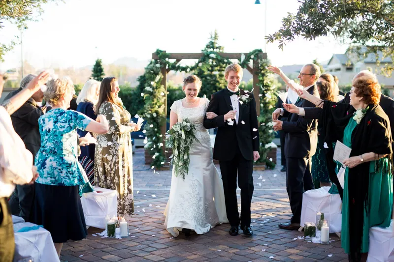Bride and groom walk out through a petal toss, a small group of guests throwing petals from both sides of a brick aisle