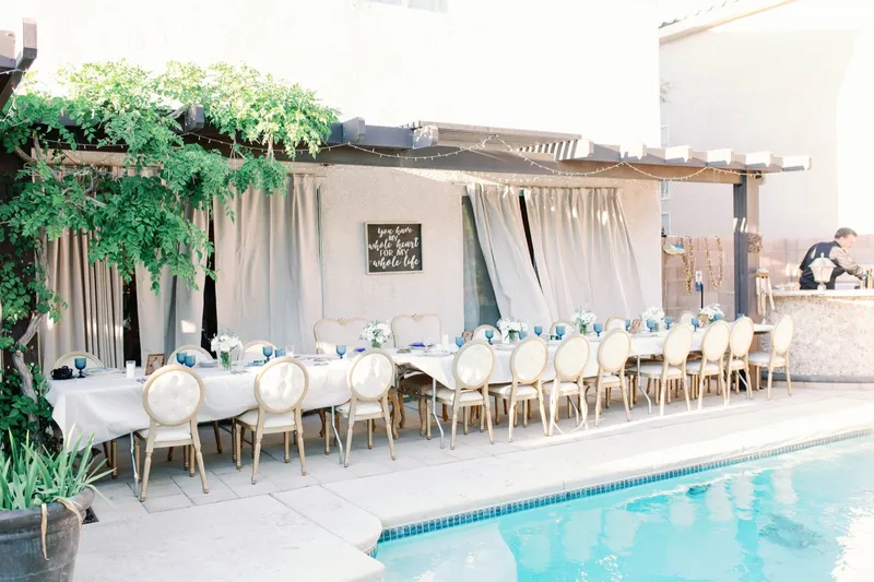 Long tables and gold chairs set along the pool deck under a draped cabana in the late afternoon