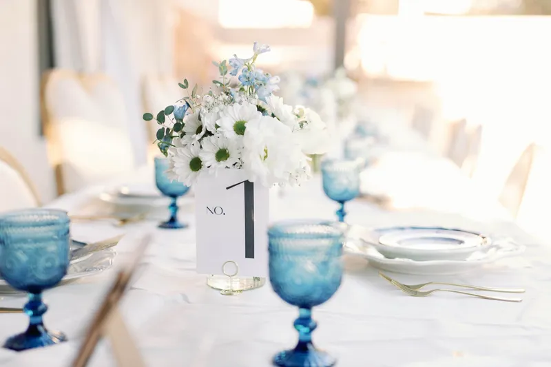 Table one marker beside a white and blue arrangement and a row of blue glass goblets