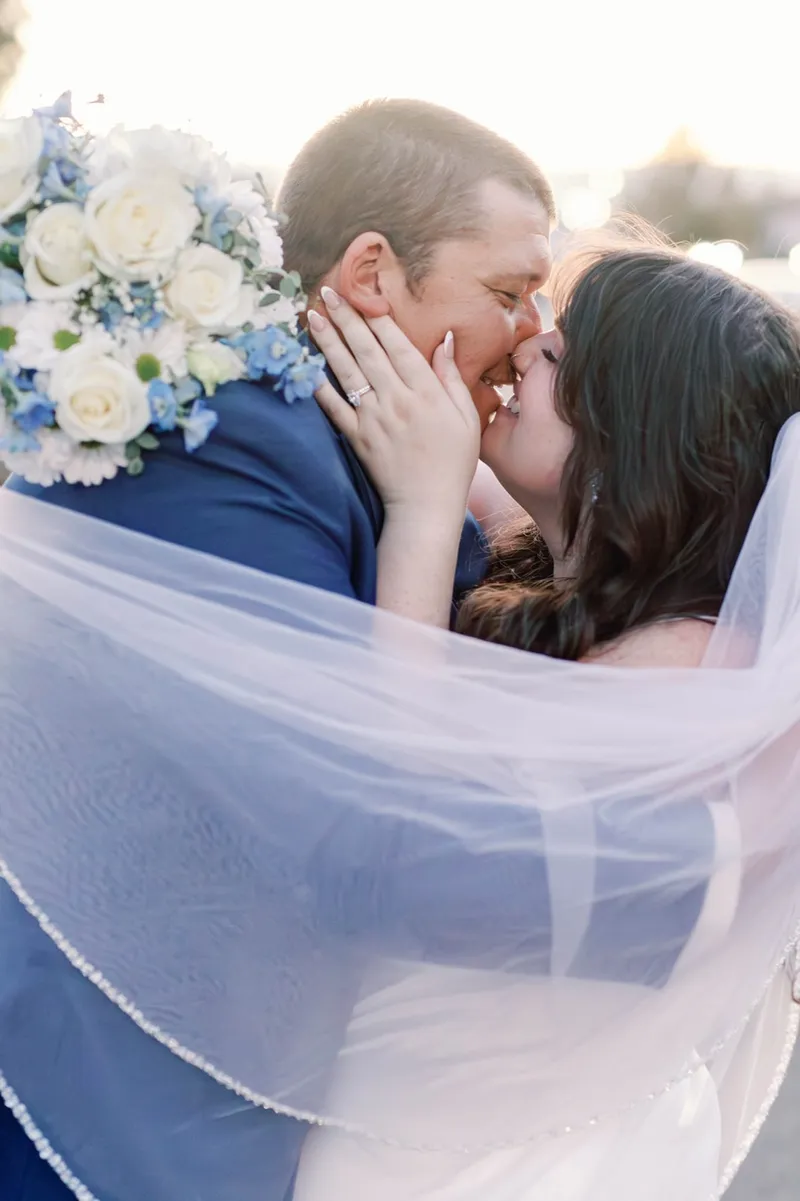 Couple kissing with the bride's veil swept around them both, the low sun coming through it