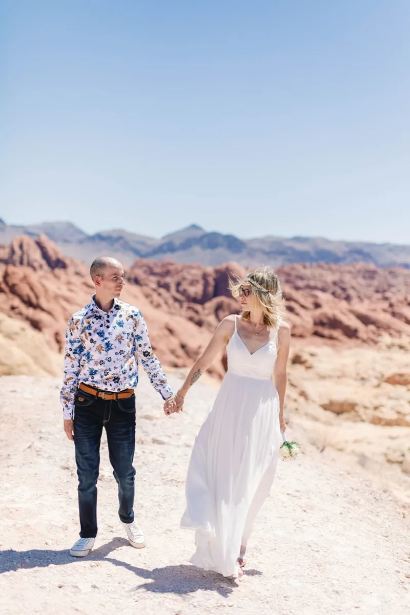 Couple walking hand in hand across the sandstone, groom in a patterned shirt and jeans