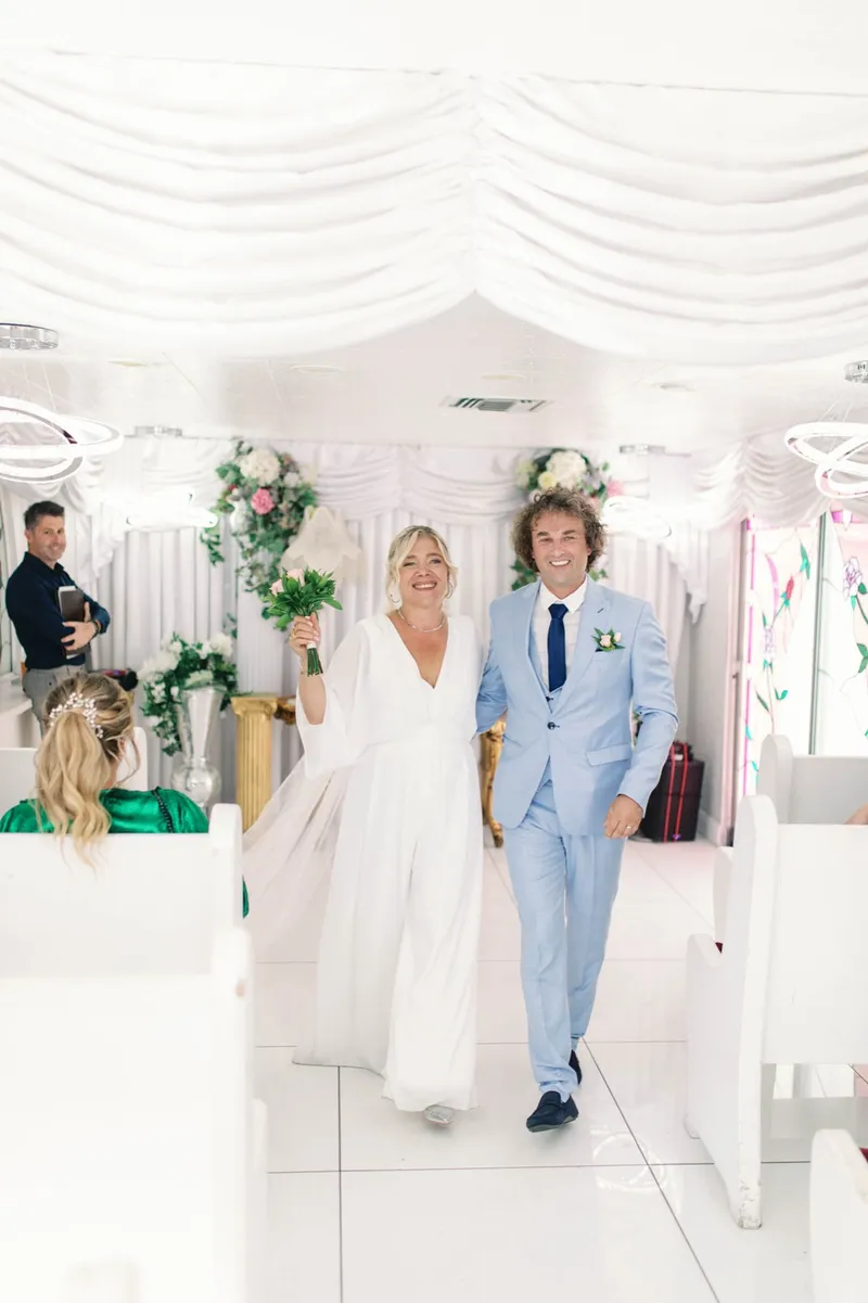 Bride raising her bouquet as she and her groom walk back down the chapel aisle