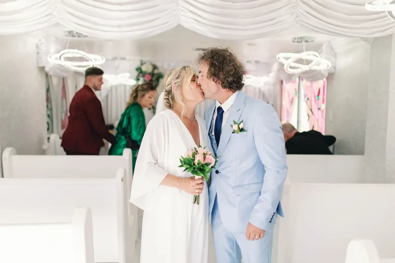 A bride and groom kissing beside the white pews inside a Las Vegas wedding chapel