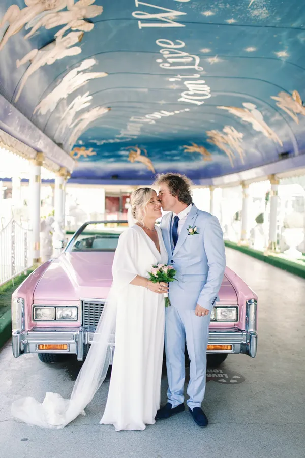 A bride and groom kissing beside the pink Cadillac at A Little White Chapel in Las Vegas