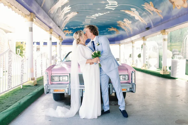 Couple kissing in front of the pink Cadillac with her long dress trailing