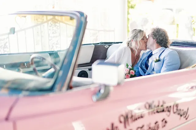 Bride and groom kissing in the back of the pink Cadillac, framed by the chapel's drive up window