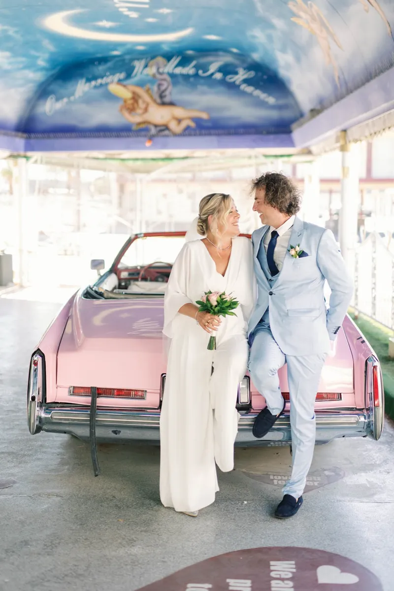 Newlyweds sitting together on the trunk of a pink Cadillac convertible at a Las Vegas chapel
