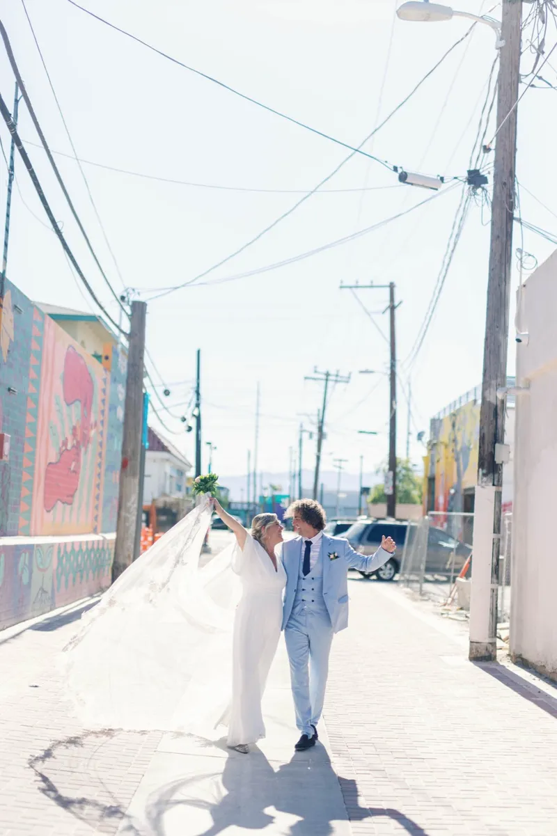 Bride and groom walking up an alley with her long veil lifting behind her and painted walls on both sides
