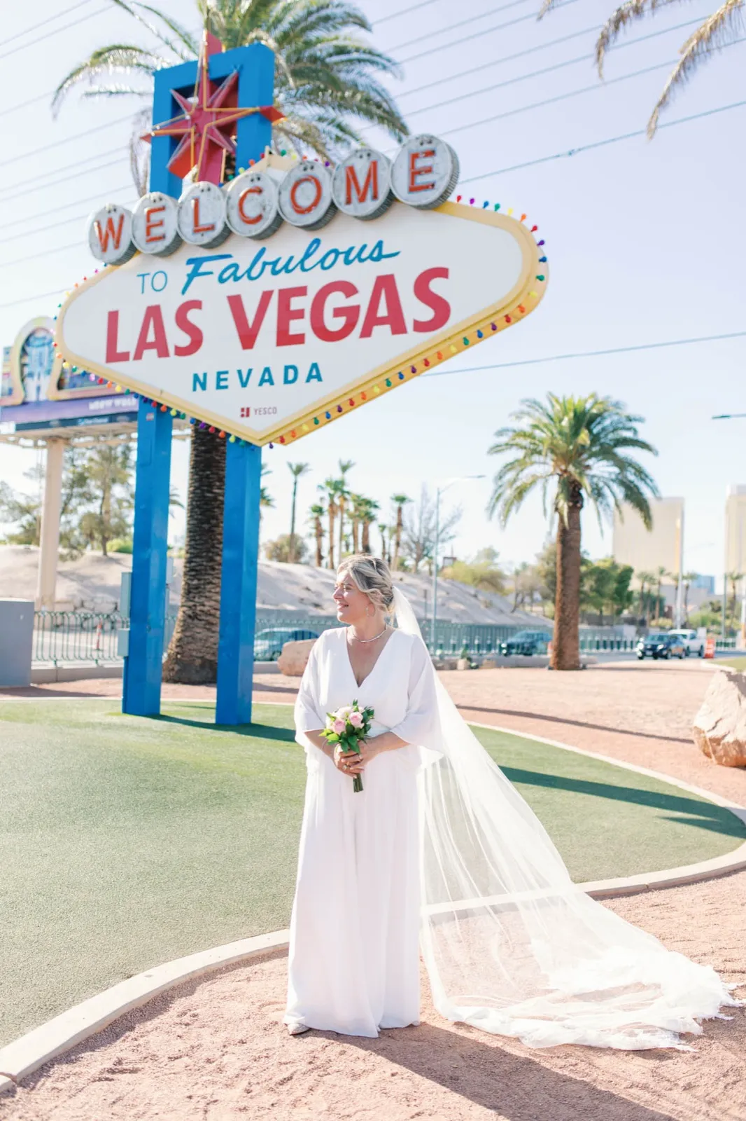 Bride alone below the Welcome to Fabulous Las Vegas sign, her long veil trailing across the empty median