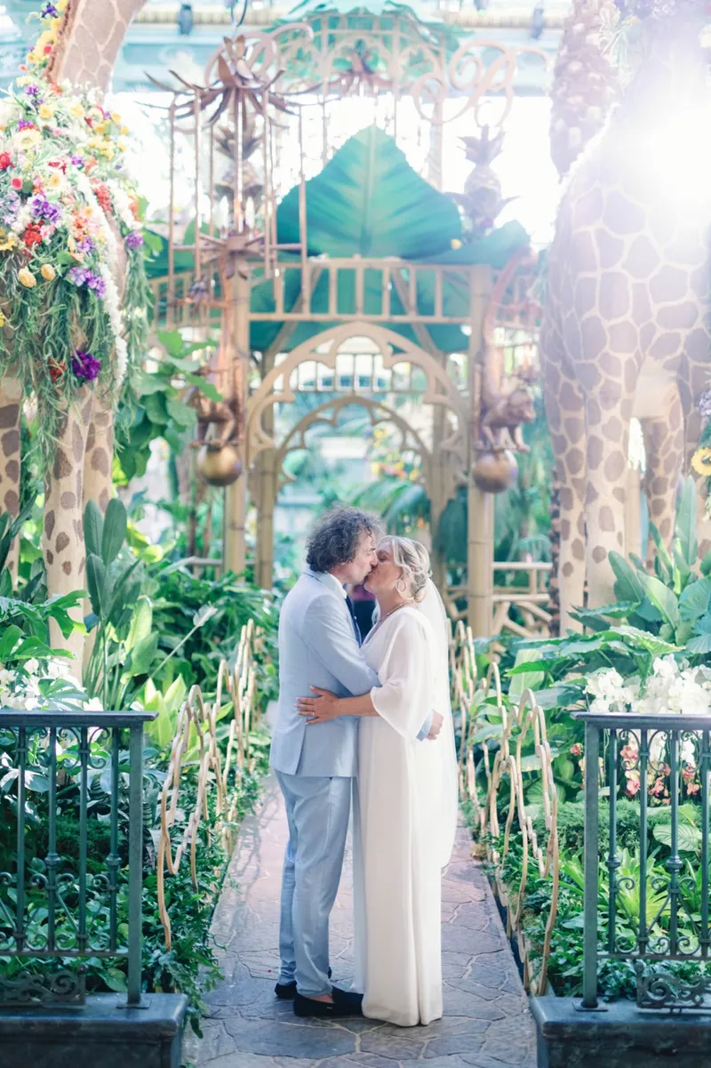 The two of them kissing inside the Conservatory surrounded by tall plants and hanging flowers