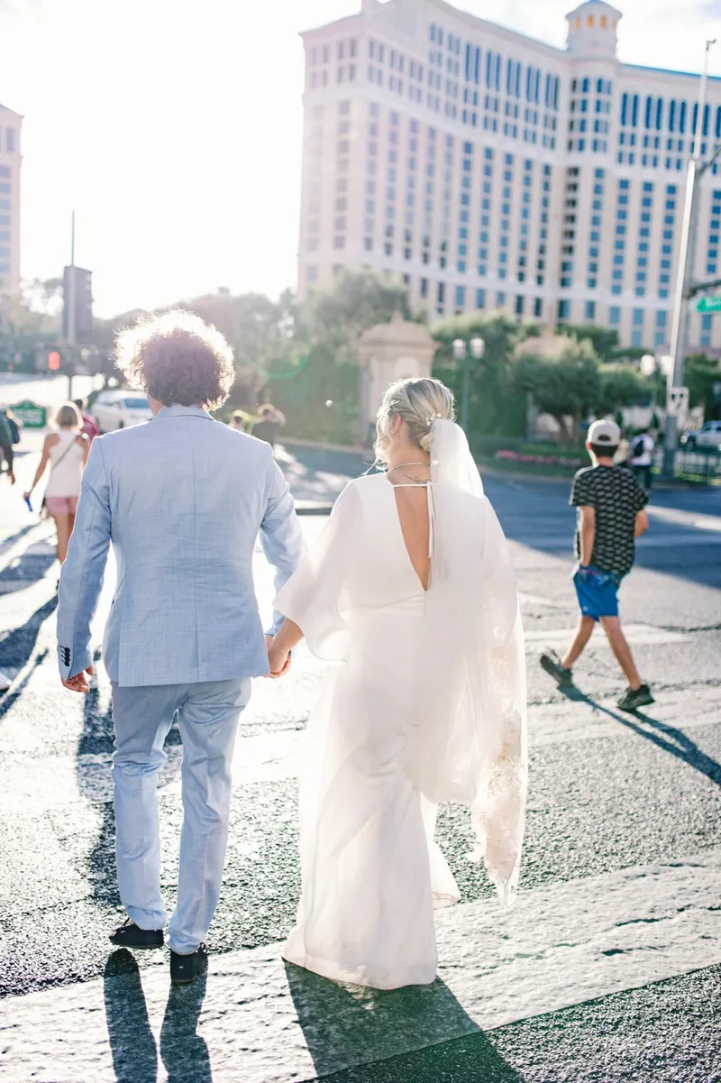 A bride and groom holding hands while crossing Las Vegas Boulevard in their wedding clothes