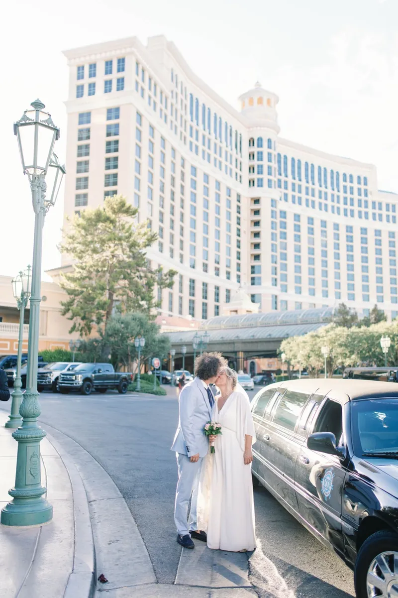 The two of them kissing beside a black stretch limousine with the Bellagio behind them