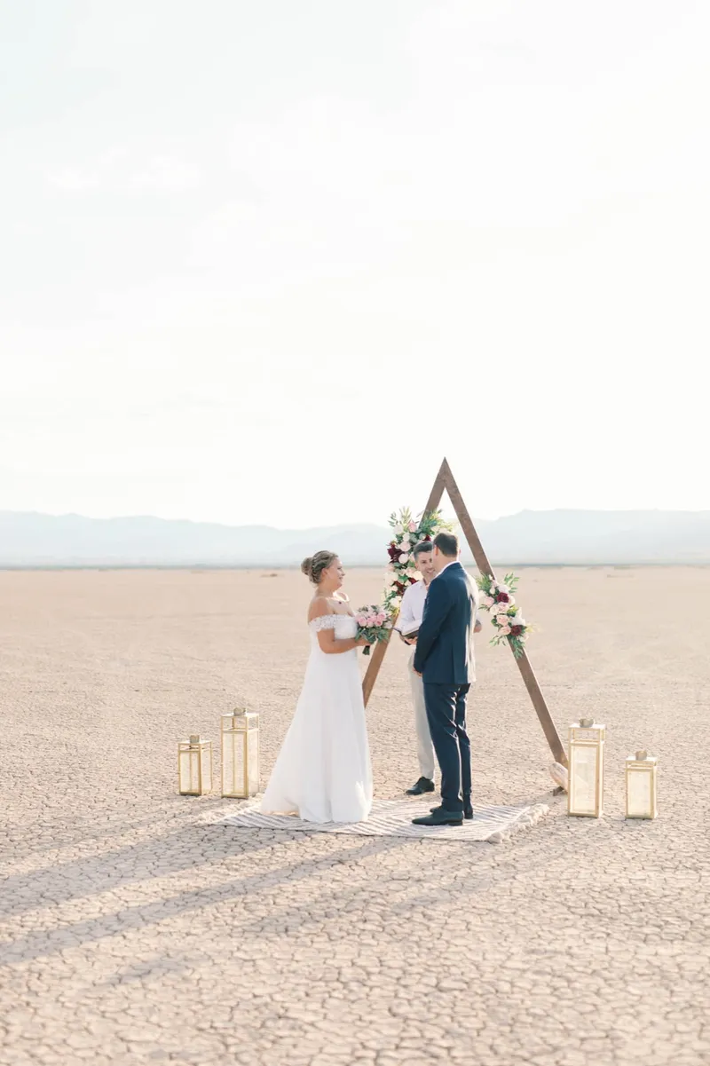 Bride and groom facing each other under the triangle arch during their ceremony on the empty flat