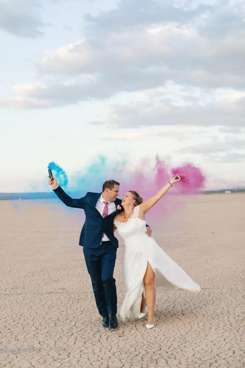 A bride and groom celebrating with blue and pink smoke on the dry lake bed outside Las Vegas