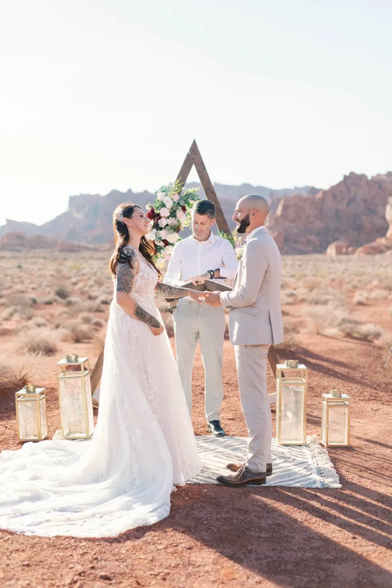 Bride and groom at a wooden triangle arch with their officiant reading between them
