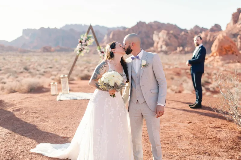 Couple kissing at the arch while a guest watches from the side