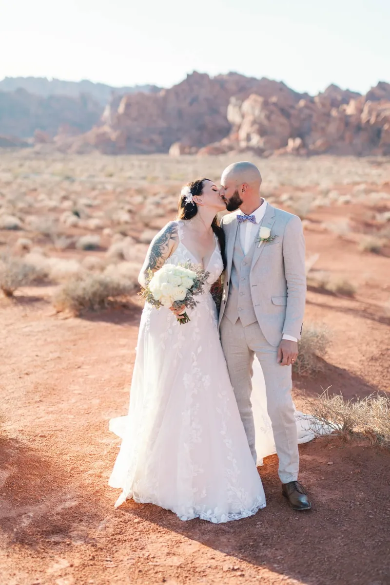 Bride and groom kissing in the desert scrub with her white bouquet between them