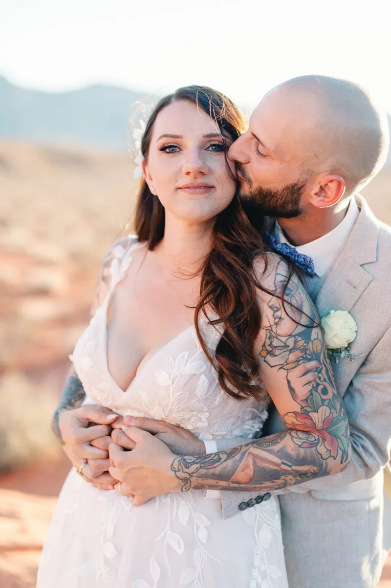 Bride with sleeve tattoos held close by her groom, both looking at the camera