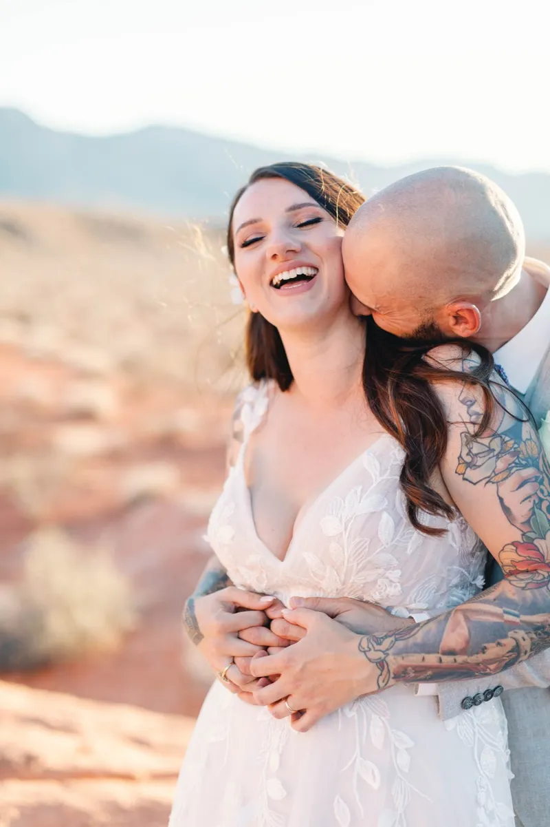 Bride laughing with her head back as her groom kisses her cheek