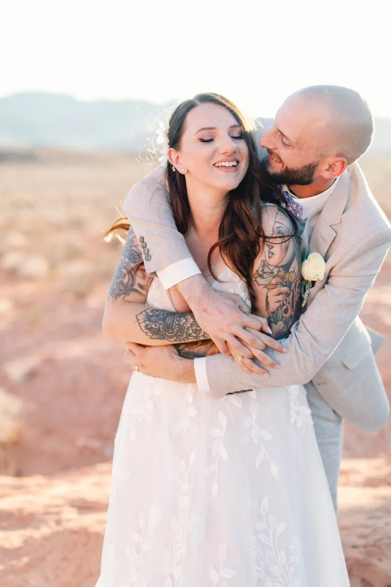 Groom wrapping both arms around his bride from behind as she looks over her shoulder
