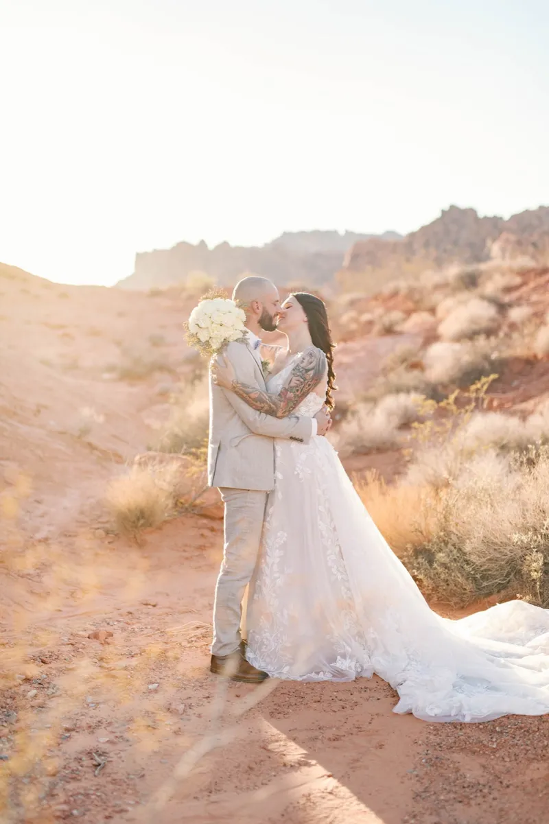 Bride and groom kissing with her bouquet raised between them in the low sun