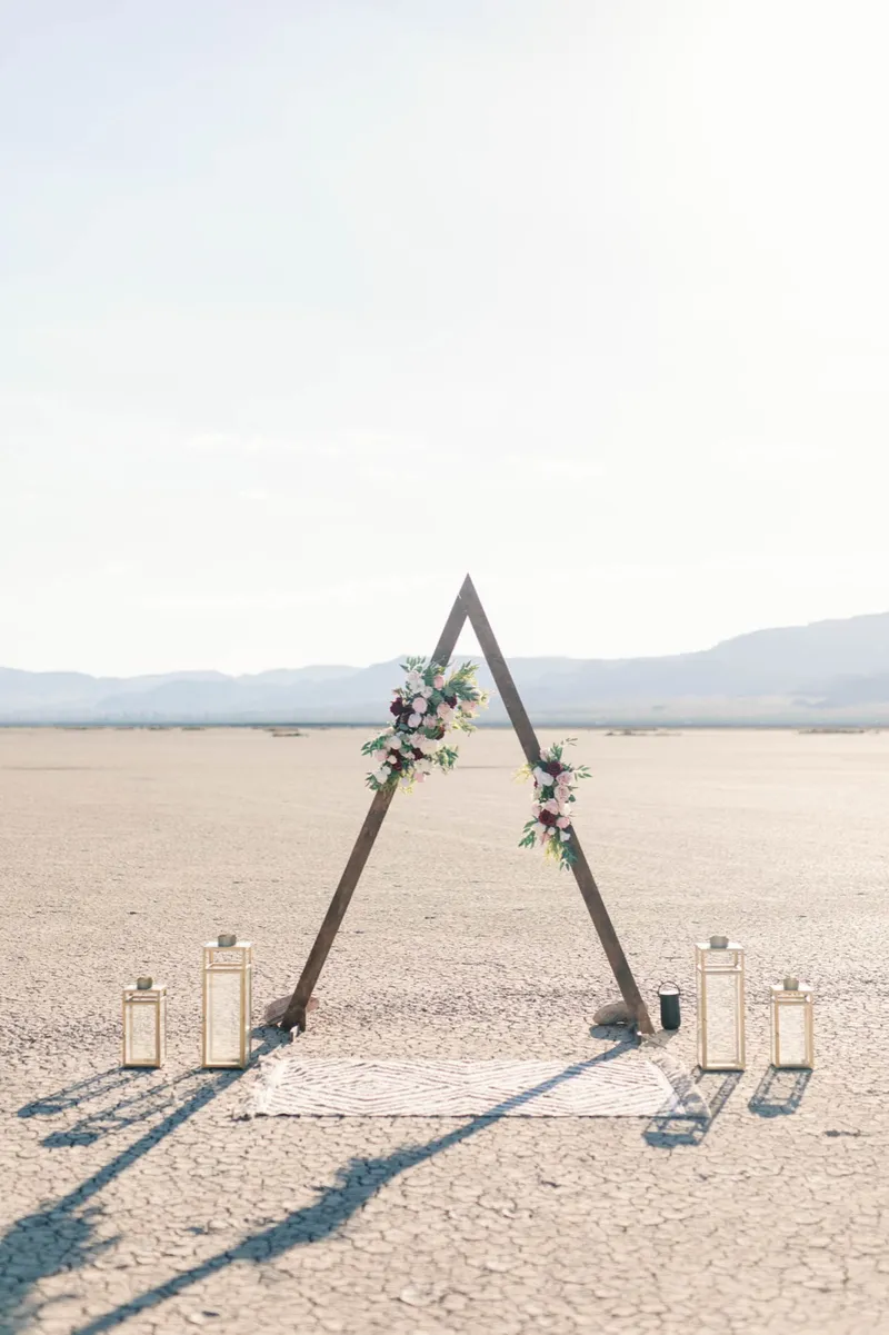 Flower covered triangle arch and gold lanterns standing empty on the flat before the ceremony