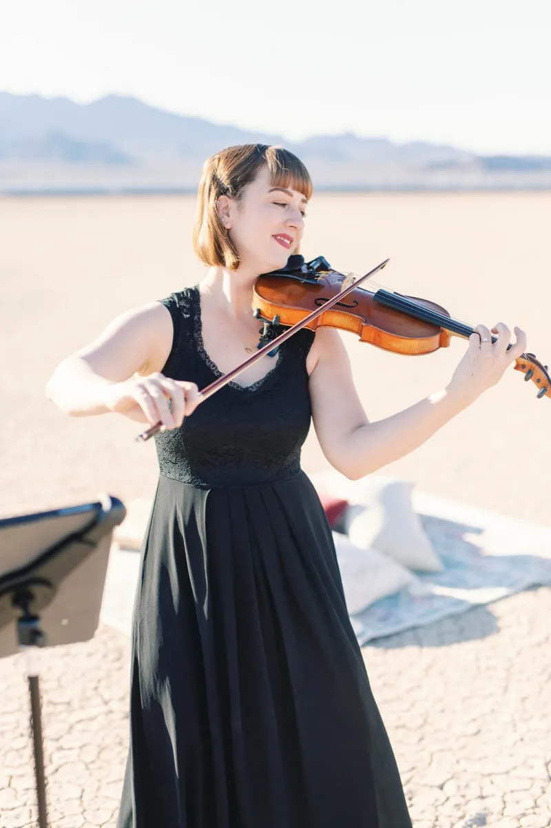 Violinist in a black gown playing her violin beside the ceremony setup on the lake bed