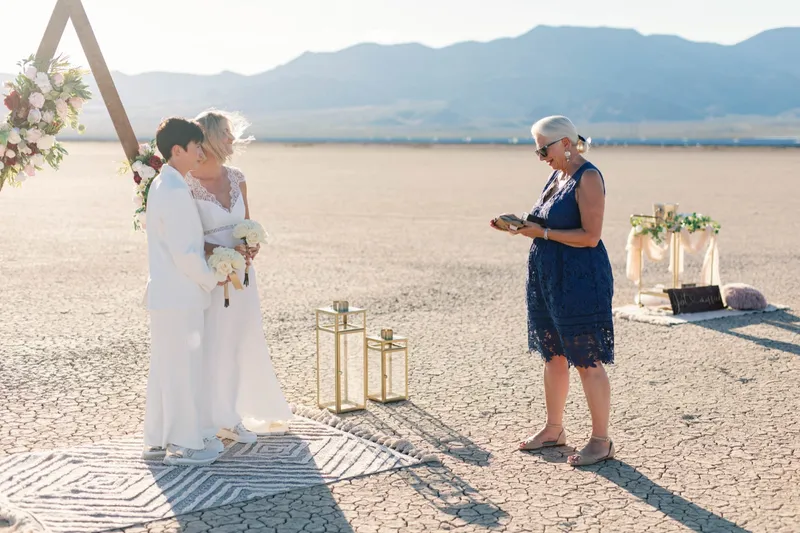 Two brides kissing at the end of their ceremony while their officiant looks on