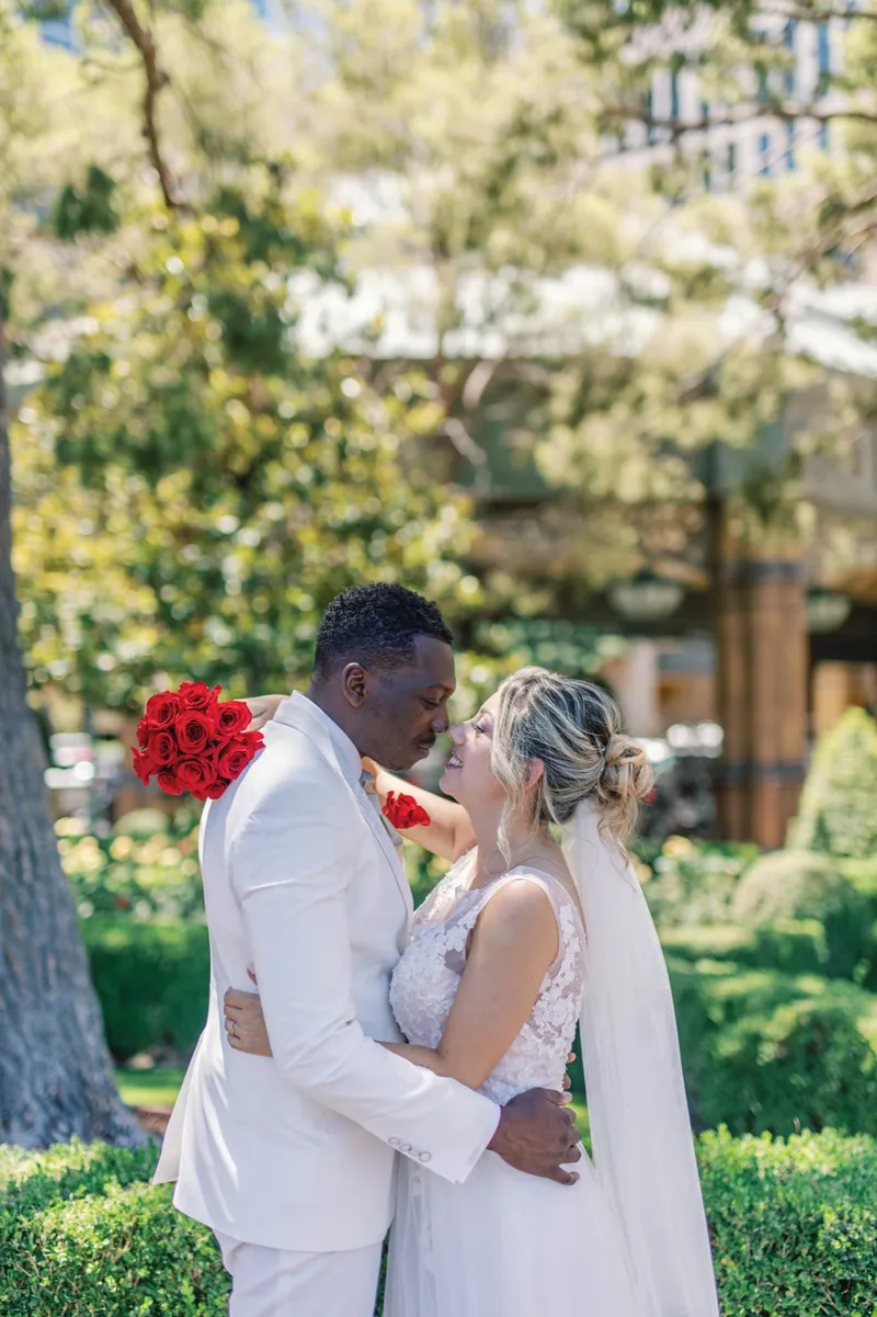 Bride and groom holding each other close with her red rose bouquet raised beside them