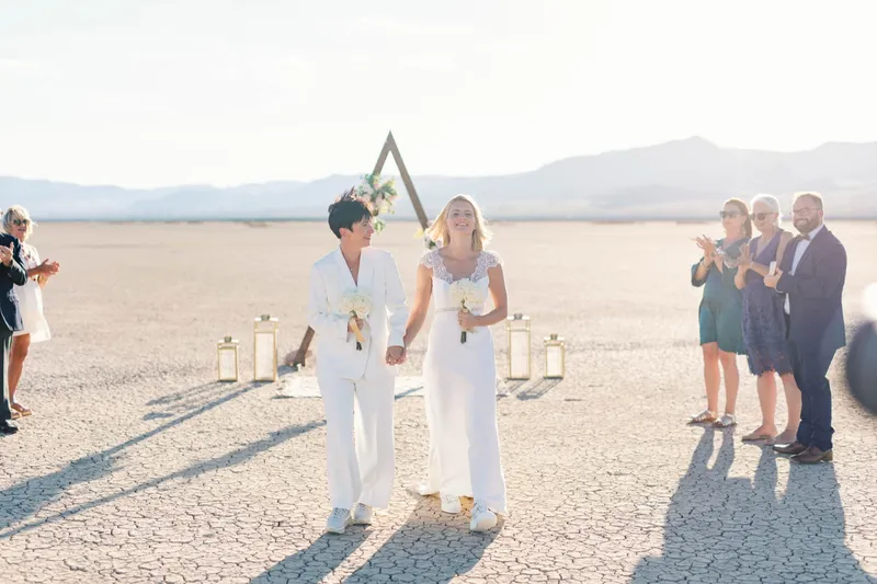 Two brides holding hands and smiling at each other during their lake bed ceremony