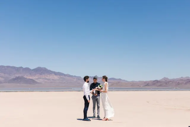 Couple standing with their officiant alone in the middle of a pale cracked lake bed with a long mountain range behind them
