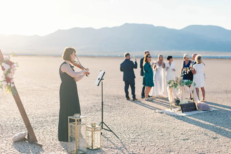 Violinist playing beside the ceremony arch while the wedding party toasts in the distance on the lake bed