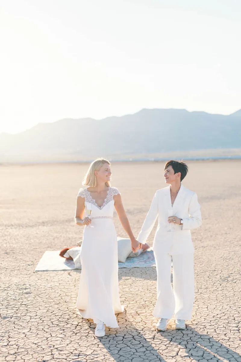 Two brides standing hand in hand on a rug spread over the cracked lake bed