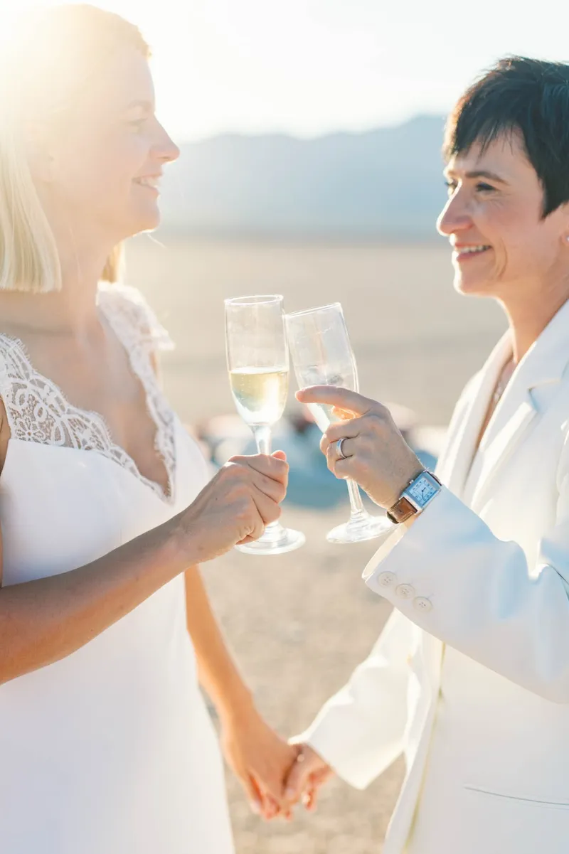 Close view of two brides clinking champagne glasses with their rings showing