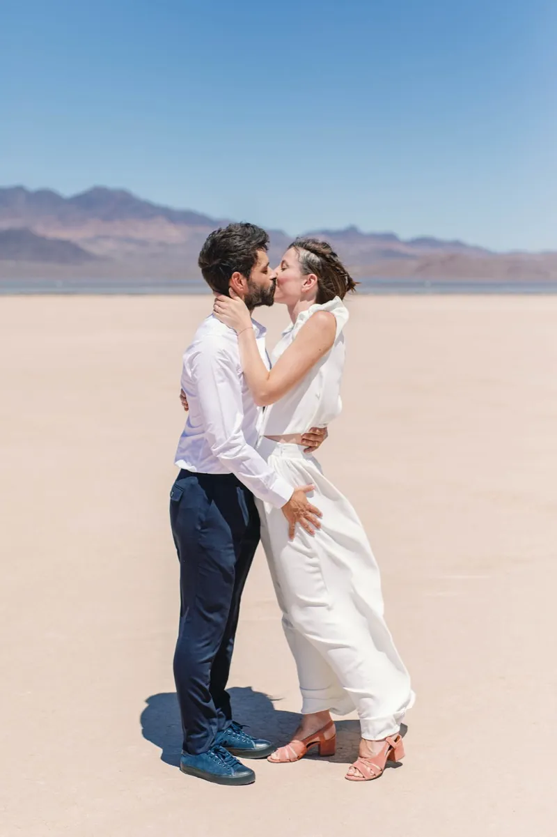 Bride and groom kissing in the open desert with the mountains soft behind them