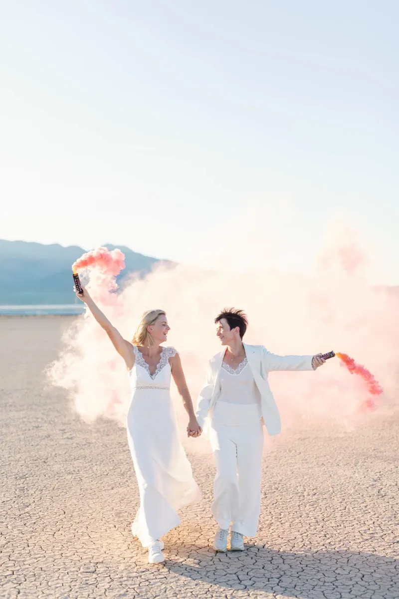 Two brides kissing with pink smoke curling around them