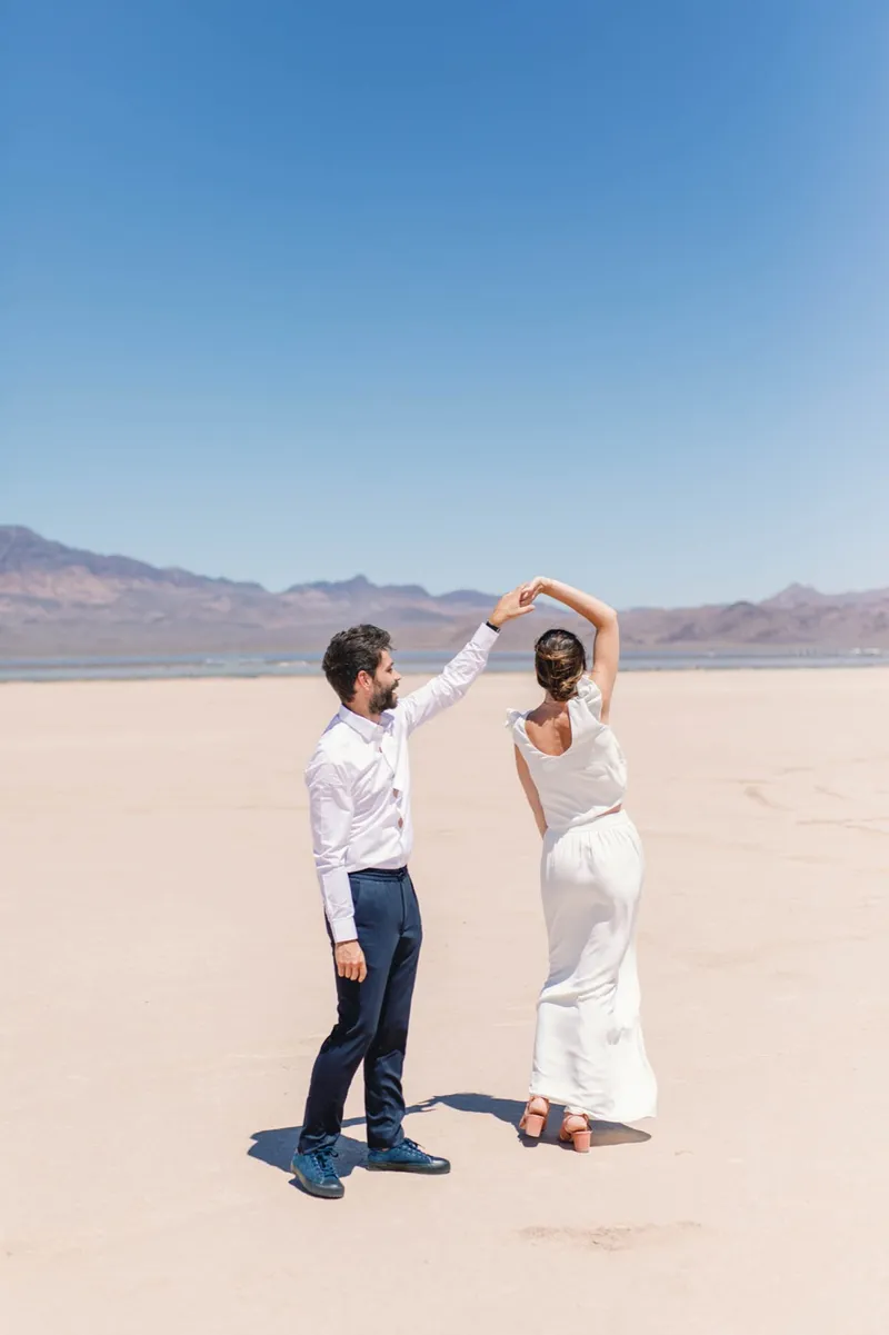 Groom spinning his bride under his arm with her white dress flaring on the lake bed