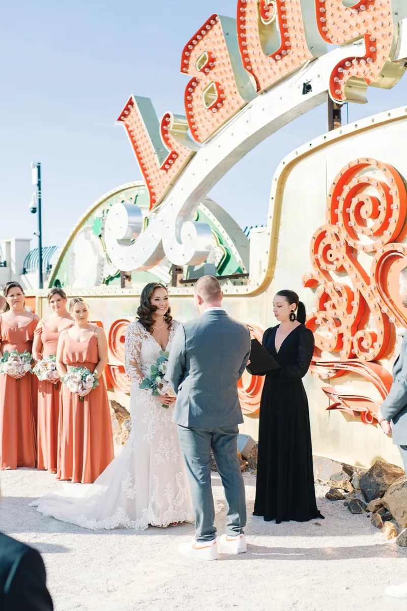 Bride and groom facing their officiant during the ceremony in front of a bright neon backdrop