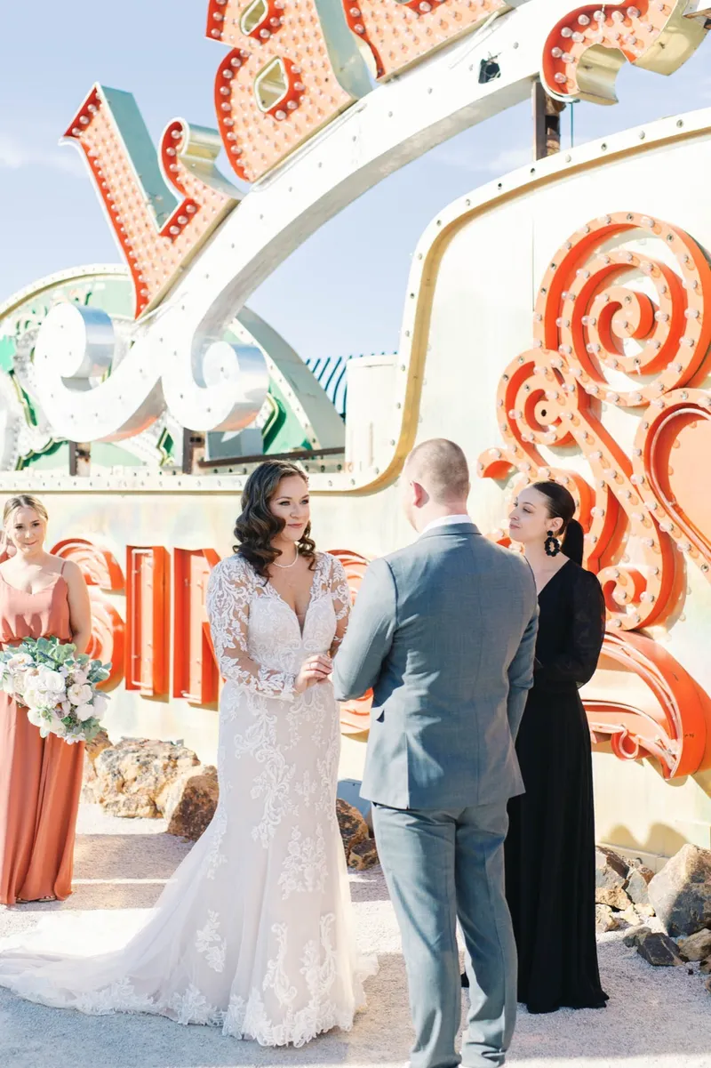 Couple holding hands during their vows with orange and cream neon behind them