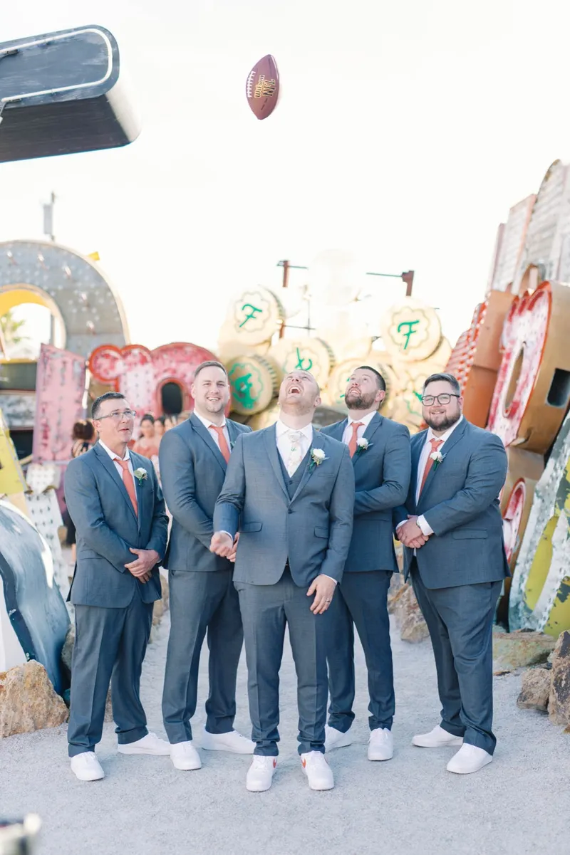 Groom and groomsmen laughing together among the neon letters