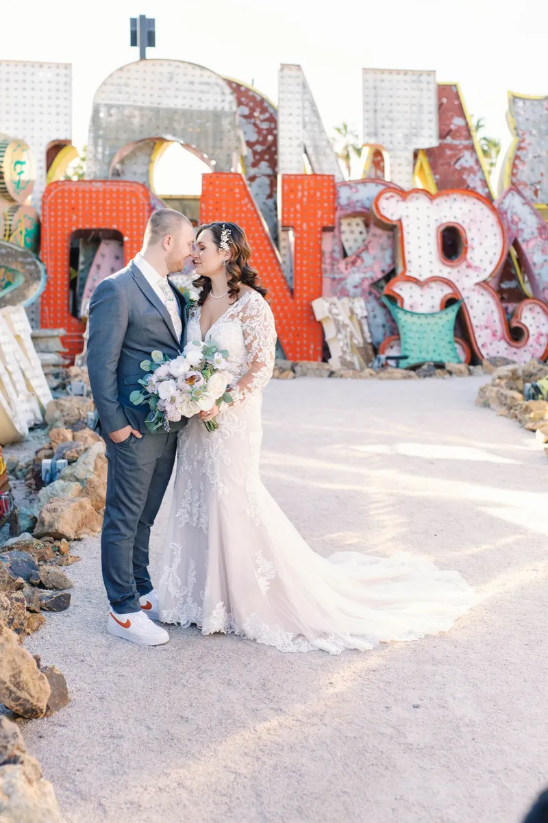 Bride and groom kissing in front of the bright neon letters with her bouquet in hand