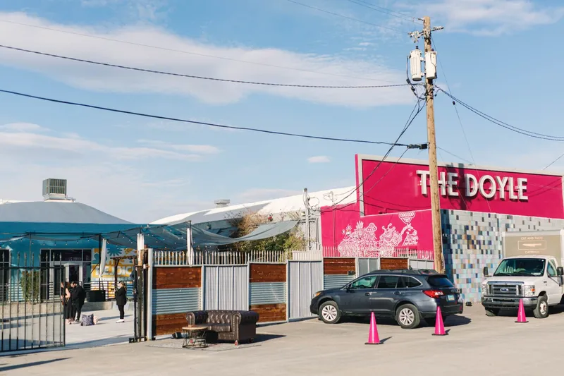 Street view of the whole building from the sidewalk, the pink sign at one end and the long curved metal roof rising behind the front gate
