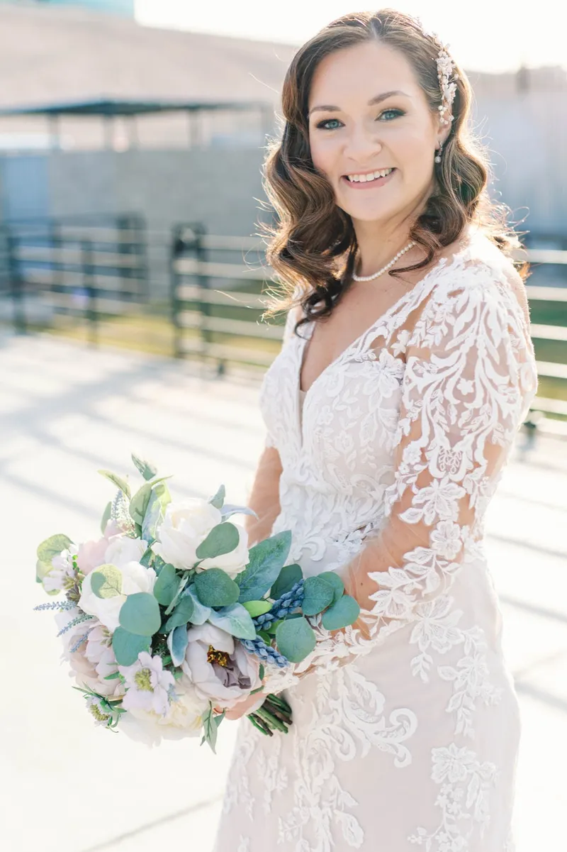Bride smiling with her bouquet held at her side, the courtyard fence and the hedge behind her going soft