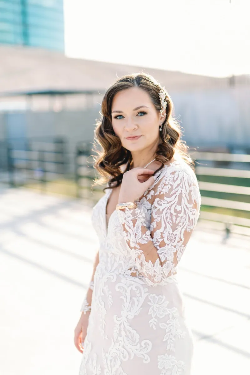 Bride with one hand at her collarbone looking straight at the camera, afternoon sun coming low across the concrete behind her
