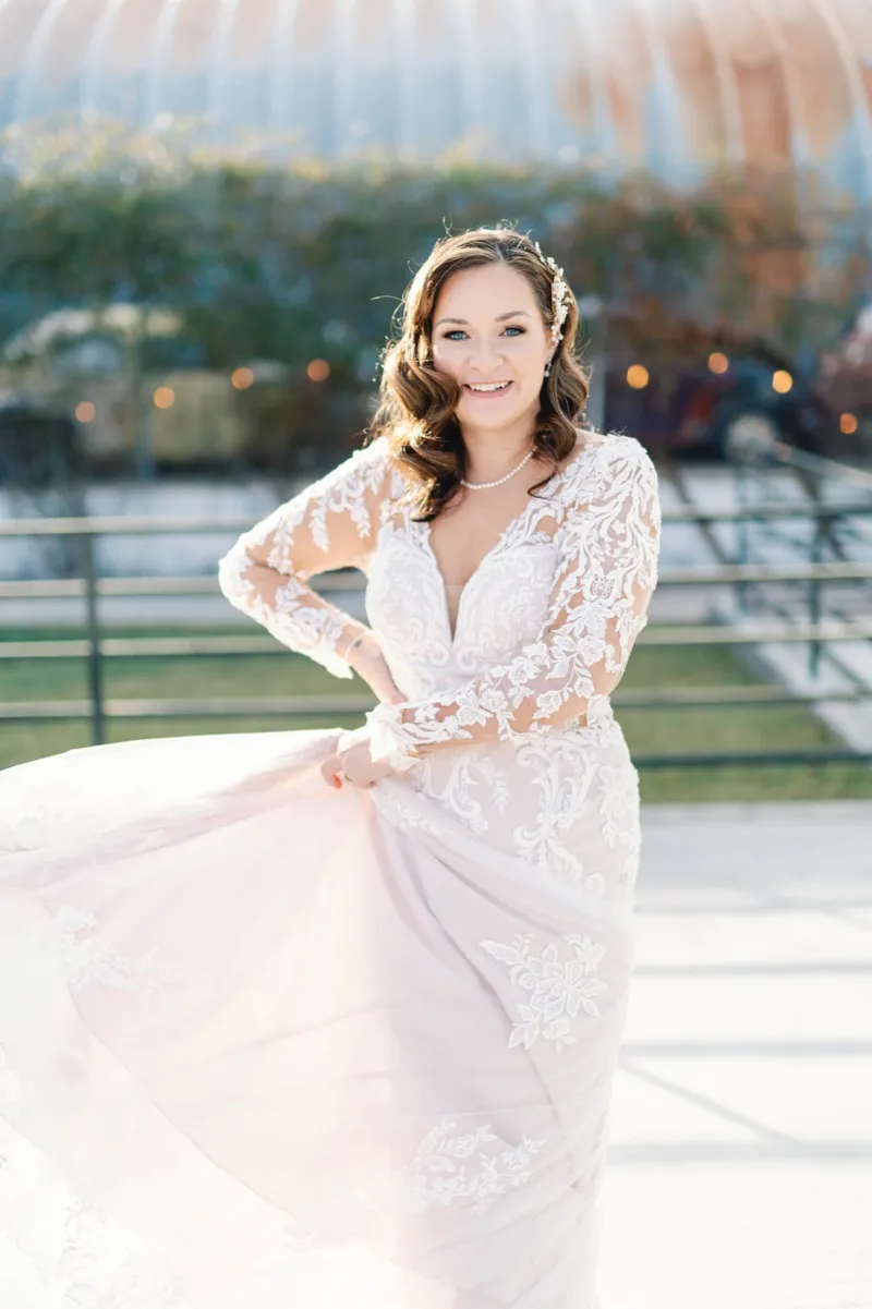 Bride holding the blush lined skirt of her gown out to one side and smiling toward the camera