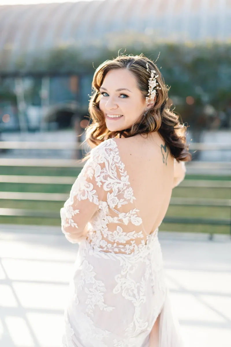 Back of the bride's sheer lace gown as she looks over her shoulder, the sun catching the lace across her shoulders