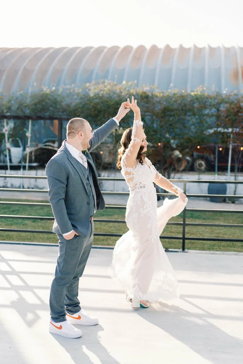 Groom turning the bride under his raised arm on the courtyard, her skirt swinging and long shadows running across the concrete